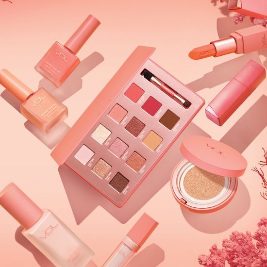This cosmetic collection ad features a flat-lay photography style with a consistent coral color theme, highlighting a palette, blush, and lipstick.