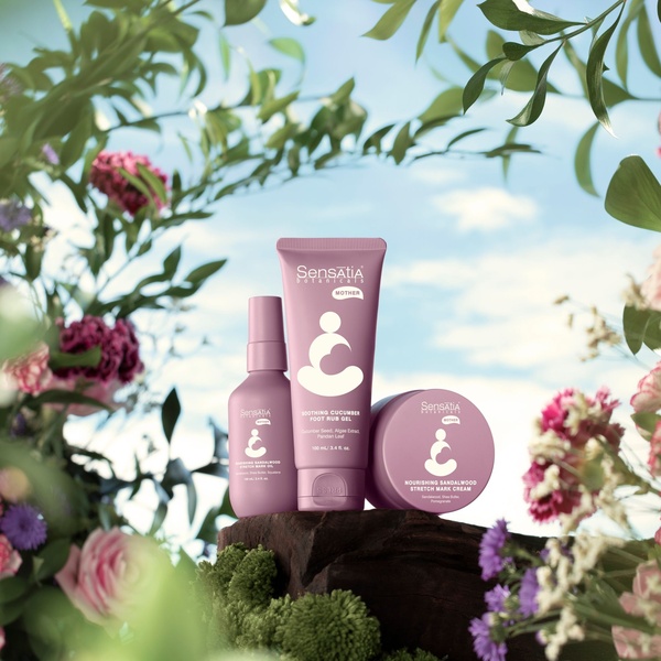A high-quality studio photography shot showcasing a set of motherhood skincare products nestled among lush, soft-focus greenery and flowers.