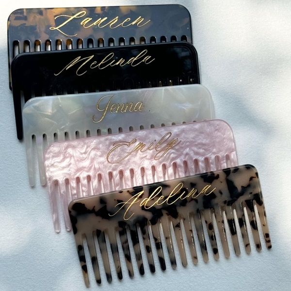 A high-contrast, overhead studio shot displaying multiple custom-engraved hair combs in varying tortoiseshell patterns.