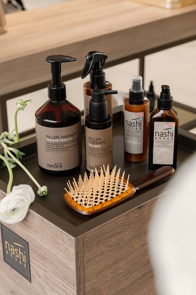 A high-quality studio shot of Nashi Argan hair care products arranged on a wooden platform, emphasizing a clean and premium brand identity.