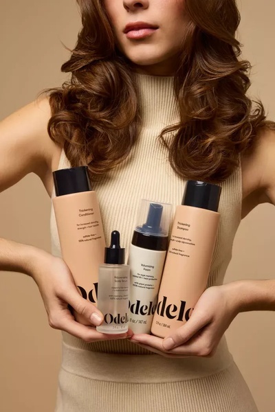 A high-quality studio shot of a model holding a curated set of thickening hair care products, highlighting a premium and professional brand identity.