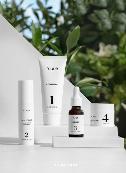 A high-end, clean product photography layout showcasing a four-step skincare set arranged on minimalist white platforms with natural foliage in the background.
