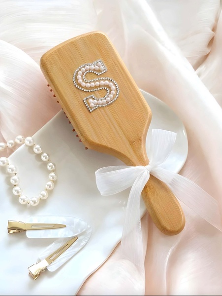 A high-end visual showcase featuring a personalized bamboo hairbrush adorned with pearls, accompanied by matching hair accessories on a neutral silk background.