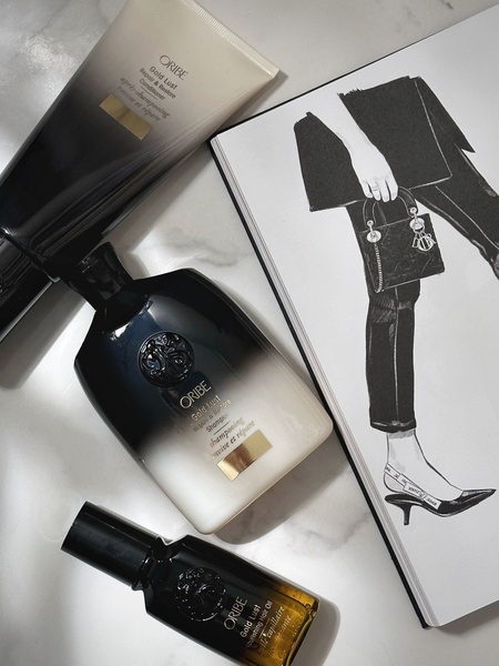 A high-end, minimalist flat-lay of three hair care bottles positioned next to an editorial sketch of a stylish woman, set on a clean marble surface.