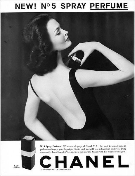 A high-contrast, black and white lifestyle photograph of a woman applying spray perfume, focusing on elegance and brand prestige.