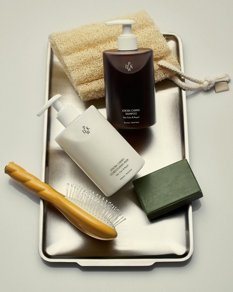 A high-end, top-down flat lay composition featuring a shampoo, conditioning mask, loofah, and brush on a sleek metal tray.