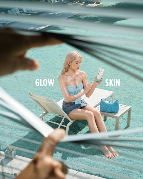 A high-angle POV shot showing a model sitting poolside with a tube of sunscreen, emphasizing radiant, glowing skin.