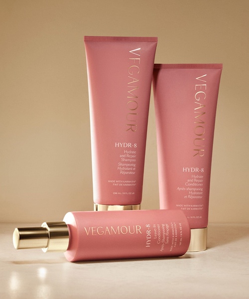 A clean, studio-lit hero shot featuring a shampoo, conditioner, and leave-in treatment bottle on a neutral beige background.