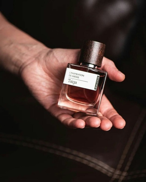 A close-up, natural perspective of a perfume bottle held in an open palm against a dark, moody background.