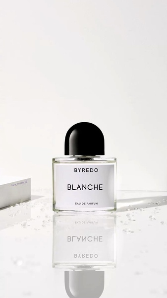 A high-key studio photograph of a perfume bottle placed on a reflective surface with scattered crystal accents, emphasizing a clean and premium brand aesthetic.