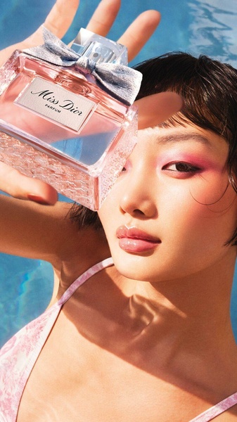 A close-up shot of a perfume bottle held against a pool background, featuring warm lighting and saturated colors to evoke a summer mood.