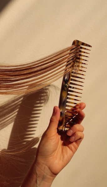 A high-contrast, vertical shot of a patterned hair comb gliding through a single section of blonde hair, emphasizing texture and quality.