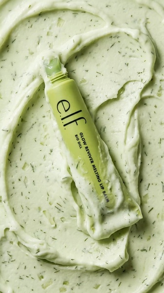 A close-up, top-down shot of a lip balm tube emerging from a thick, green, dill-speckled balm texture.