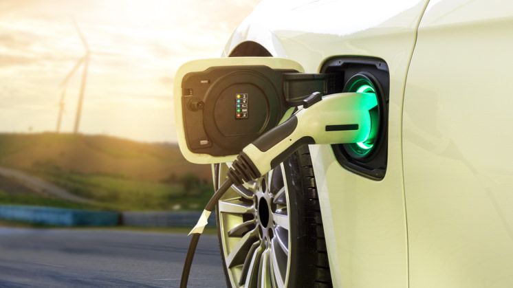 A close-up shot of an electric vehicle charging station with a wind turbine background, emphasizing clean energy.