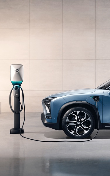 A high-end, clean studio shot featuring an electric vehicle connected to a modern wall-mounted charging station. The image emphasizes professional design and sustainability.