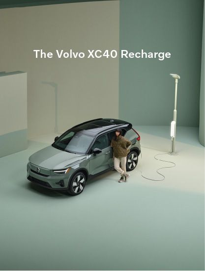 A high-end, minimalist lifestyle shot featuring an electric SUV parked indoors with a person leaning against it, emphasizing clean lines and soft earth tones.