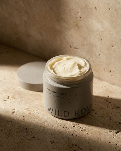 A high-quality, close-up hero shot of a body moisturizer jar resting on a textured stone surface, emphasizing organic ingredients and luxury minimalism.