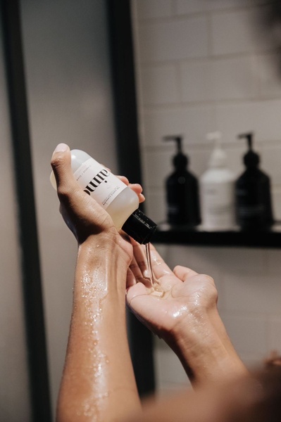 A close-up, high-quality shot of a facial cleanser bottle being poured into a hand to showcase product consistency and tactile quality.