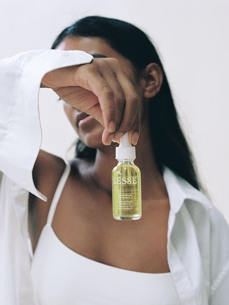 A close-up, soft-focus shot of a model holding a facial serum bottle, obscuring their face to focus attention entirely on the product packaging.