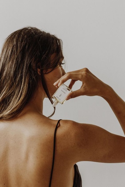 A close-up, high-key shot of a woman applying a luxury perfume oil, emphasizing a serene, personal, and premium aesthetic.