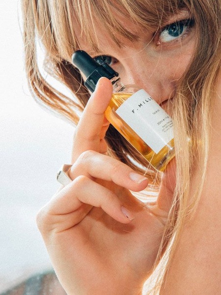 A close-up, intimate photograph of a model holding a bottle of face oil near her eye, emphasizing natural beauty and product authenticity.