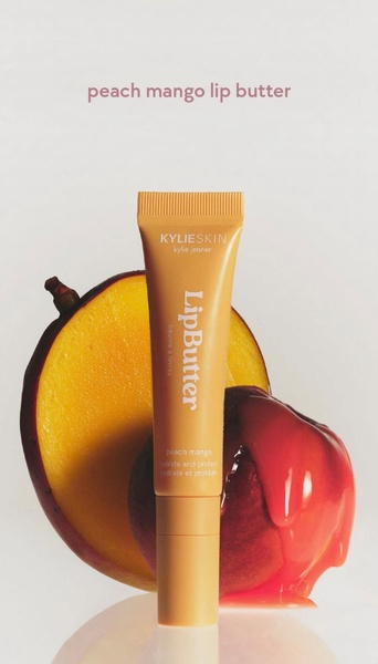 A clean, studio-lit close-up shot of a peach mango lip butter tube centered in front of a sliced mango, evoking a fresh, fruit-forward sensory experience.
