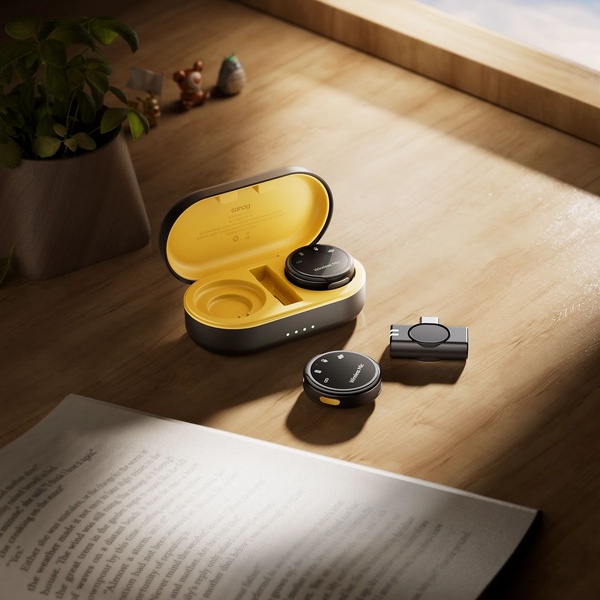 A high-quality, top-down product shot of a wireless microphone system in its open charging case, displayed on a warm, sunlit wooden desk.