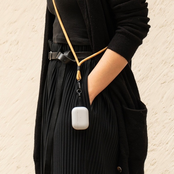 A close-up lifestyle shot of a person wearing a beige carrying case for wireless earbuds, styled against a black outfit for contrast.