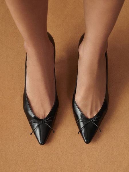 A close-up, top-down perspective focusing on the clean lines, texture, and elegant bow detailing of a pair of black ballet flats.