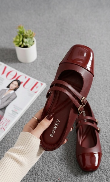 A high-angle handheld shot of a deep burgundy Mary Jane flat, emphasizing texture and design against a neutral background.