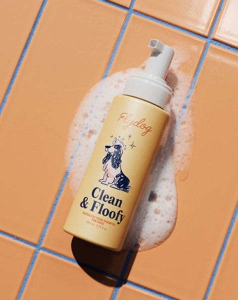 A high-quality, studio-style shot of a waterless dog shampoo bottle placed on warm-toned tiles with active foam elements, emphasizing product texture and clarity.