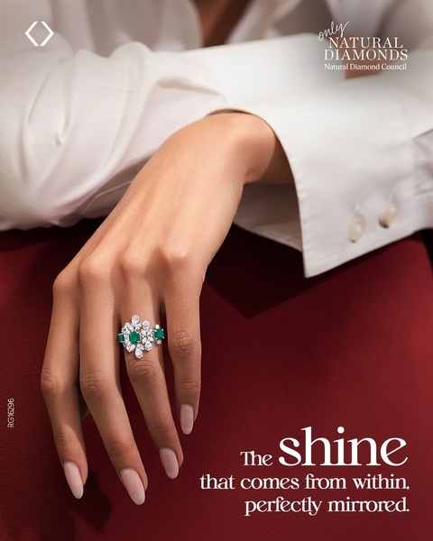 A close-up, high-fashion lifestyle photograph of a hand wearing an intricate diamond and emerald ring with elegant, sparse typography.