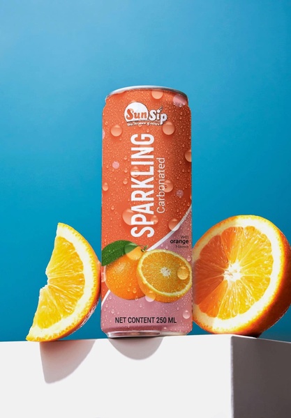 A high-contrast studio shot of a 250ml sparkling orange soda can, featuring fresh orange slices and water droplets against a bright blue backdrop.