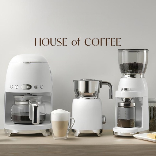 A high-end, clean studio shot of a coffee maker, milk frother, and bean grinder set against a neutral wall with minimal text overlay.