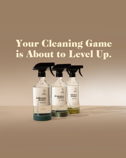 A high-contrast studio shot of three plant-powered cleaning spray bottles against a warm, neutral background with simple, aspirational typography.