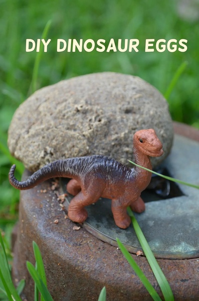 A close-up, organic image of a dinosaur toy egg next to a small dinosaur figurine in a natural, grassy setting.