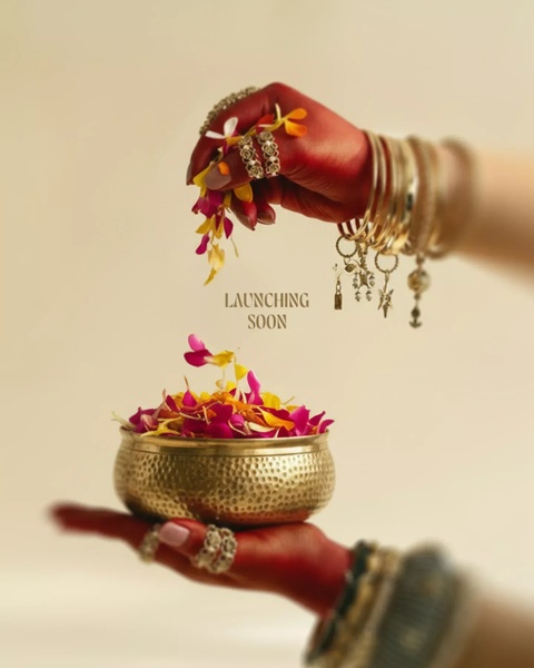 This creative displays a high-end, artistic reveal for jewelry. It features hands adorned with gold bangles and rings, artfully showering flower petals into a brass bowl to signify a luxury launch.