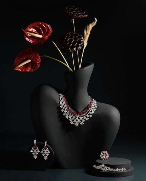 A high-end jewelry set featuring a necklace, earrings, and ring displayed on a dark, sculptural bust against a dramatic floral backdrop.