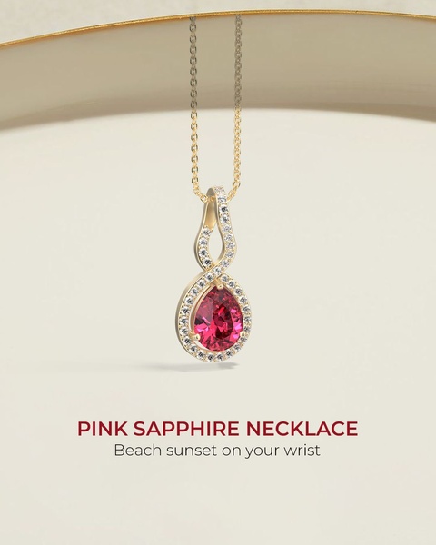 A high-end, clean product shot of a pink sapphire necklace featuring a pear-shaped gemstone set in a gold twisted halo setting.