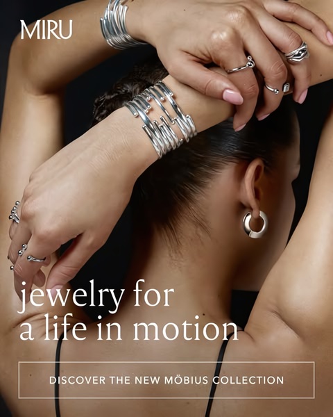 A close-up, high-fashion shot of a person wearing multiple silver rings and bracelets, emphasizing movement and elegant textures against a dark background.