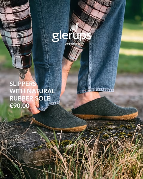 A close-up of a person wearing woolen slippers with a natural rubber sole, photographed outdoors on a rugged surface to emphasize comfort and durability.
