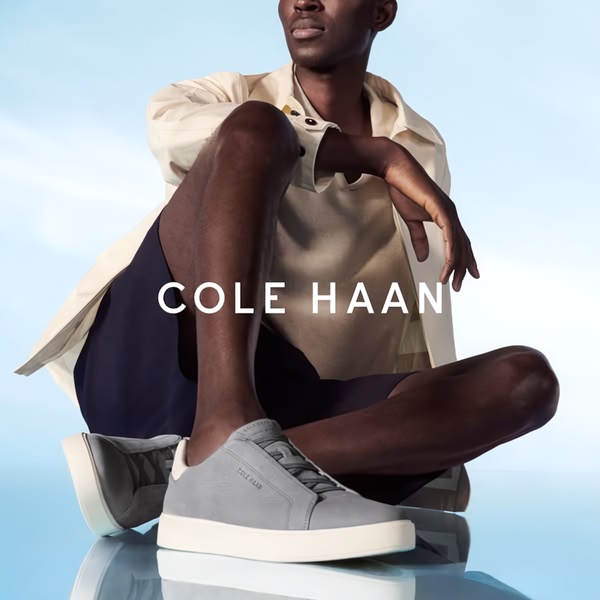 A high-key, professional studio shot of a model wearing suede sneakers, featuring clean typography and a reflective surface for a premium aesthetic.