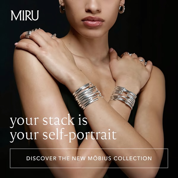 A close-up of a model wearing multiple silver bracelets, featuring a minimalist design and reflective brand photography.