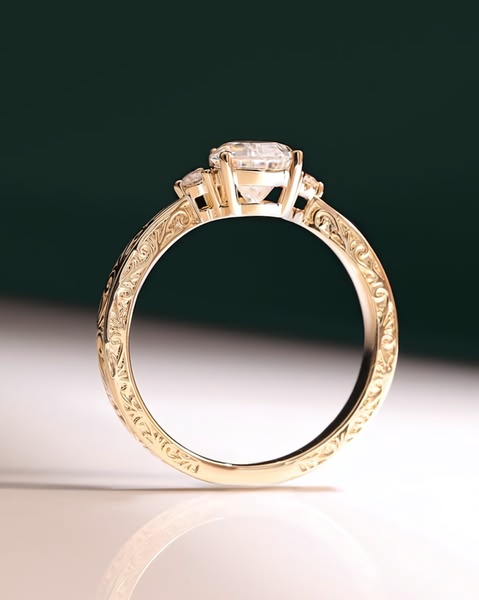 A close-up product shot of a gold ring with intricate filigree details resting on a reflective surface against a deep green backdrop.