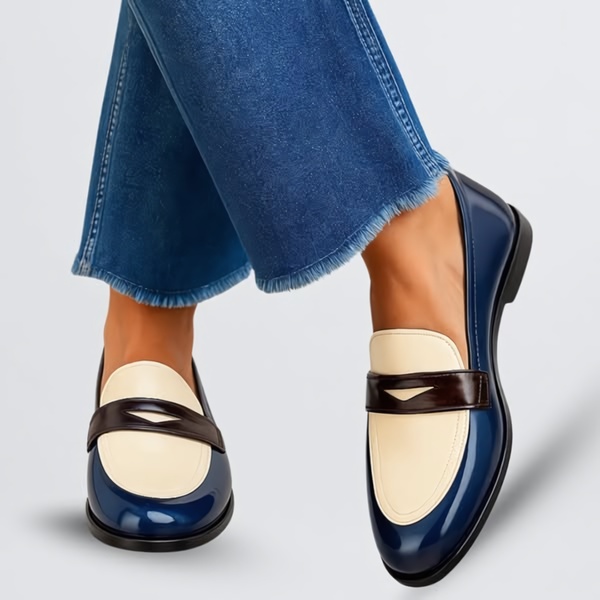 A clean, studio-lit close-up of a pair of two-tone loafers worn with cuffed denim, emphasizing the shoe's material, contrast, and style.