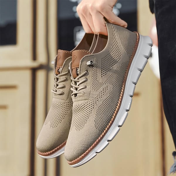 A close-up, high-clarity product hero shot showcasing the texture and neutral earth tones of a casual knit sneaker held by hand.