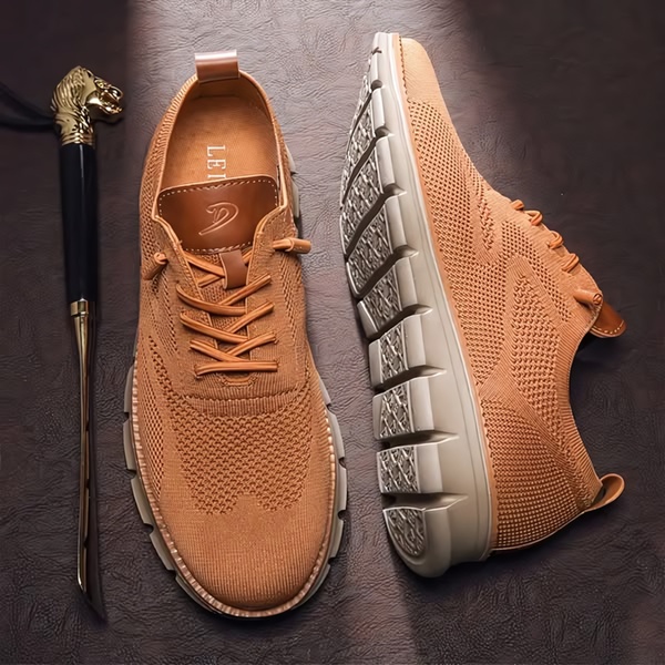 A high-angle, symmetrical product hero shot of a tan knitted sneaker paired with a luxury shoehorn on a textured dark background.