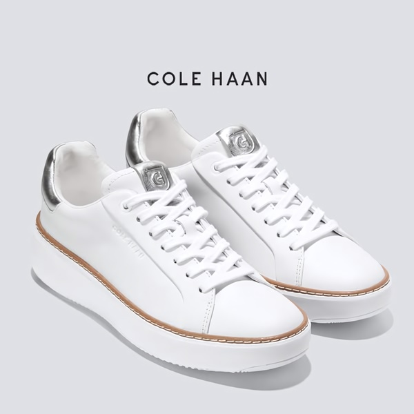 A high-fidelity studio shot of a pair of clean white sneakers with metallic accents, isolated against a neutral grey background to emphasize product design.