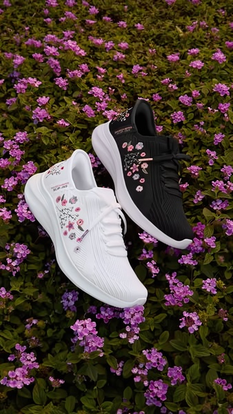 A vertical 9:16 product hero shot featuring two pairs of floral-patterned sneakers placed within a dense patch of blooming purple flowers.