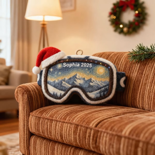 A high-quality 1:1 image featuring a personalized ski goggles ornament resting on a warm, textured sofa, complete with a Santa hat.